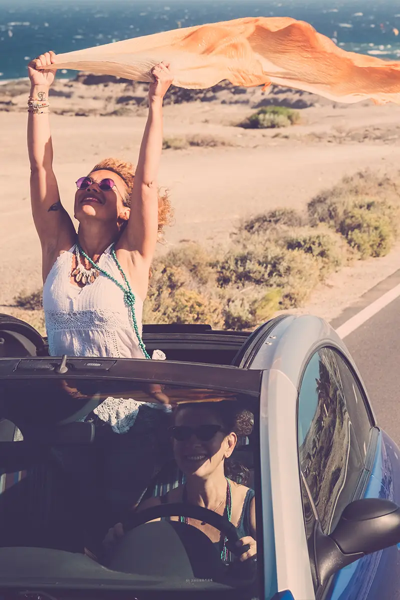 Zwei Frauen fahren entlang der Küste mit einem Auto und genießen ihre Freiheit